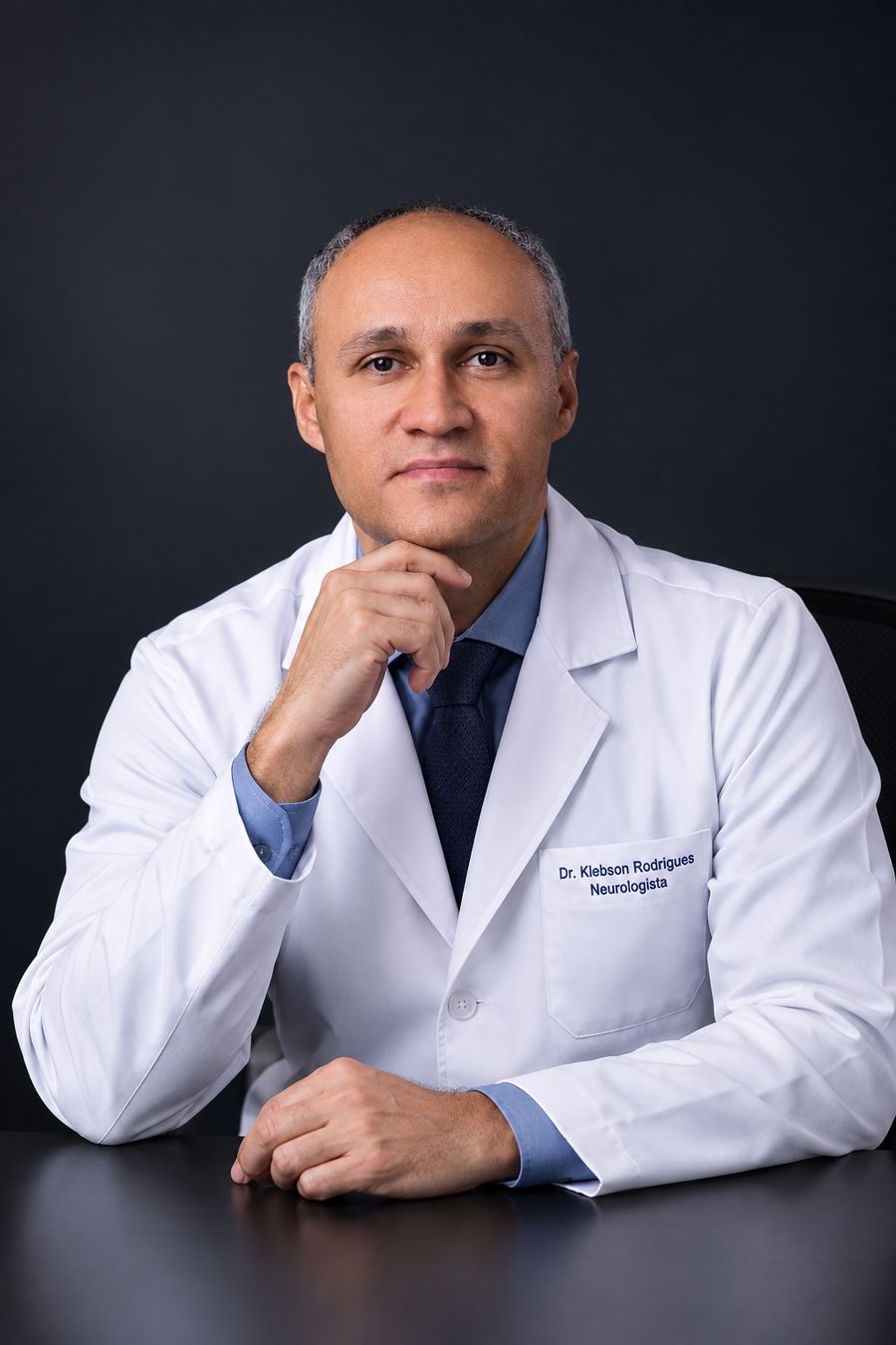 Dr. Klebson Rodrigues, neurologista, de jaleco, com a mão no queixo